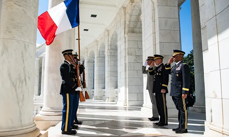  A solemn memorial hall inside a military museum, with a large wall engraved with soldiers’ names and photos, a wreath and American flags in front, soft warm lighting creating an atmosphere of reflection and respect. No people present in the scene.